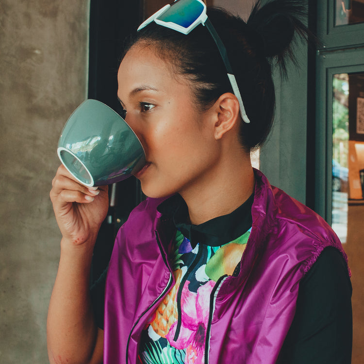 girl sipping on coffee wearing cycling glasses, jersey and gillet